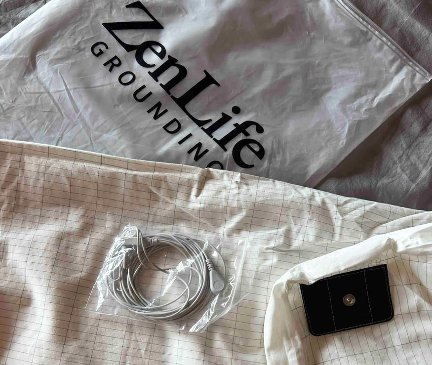 Plastic bag with 'ZenLife GROUNDING' text, a coiled cable, and a small black box on a checked fabric.