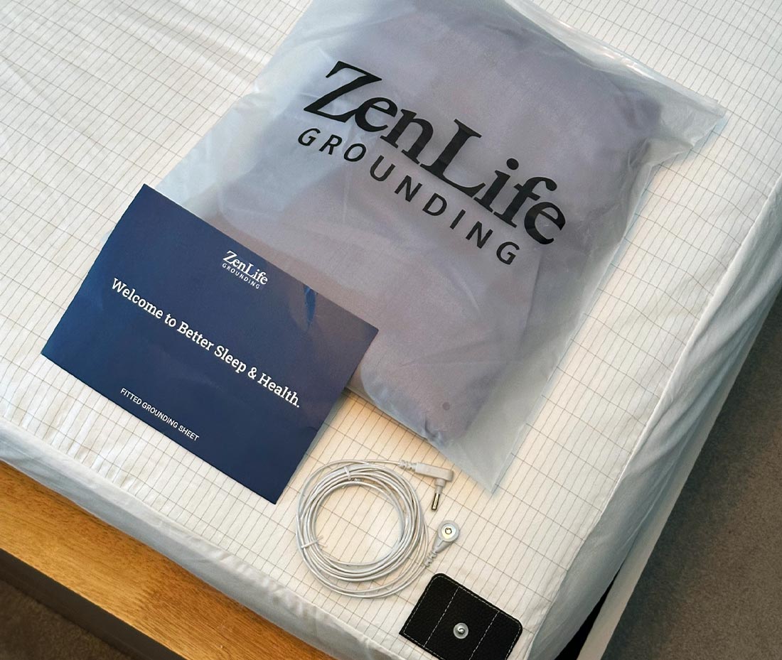 A ZenLife grounding sheet package on a bed with an instruction card and a grounding cord.
